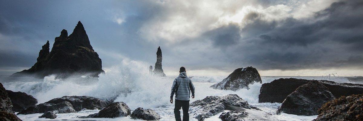 Mann steht vor wildem Meer im Hintergrund Felsen und atmosphärisches Licht 